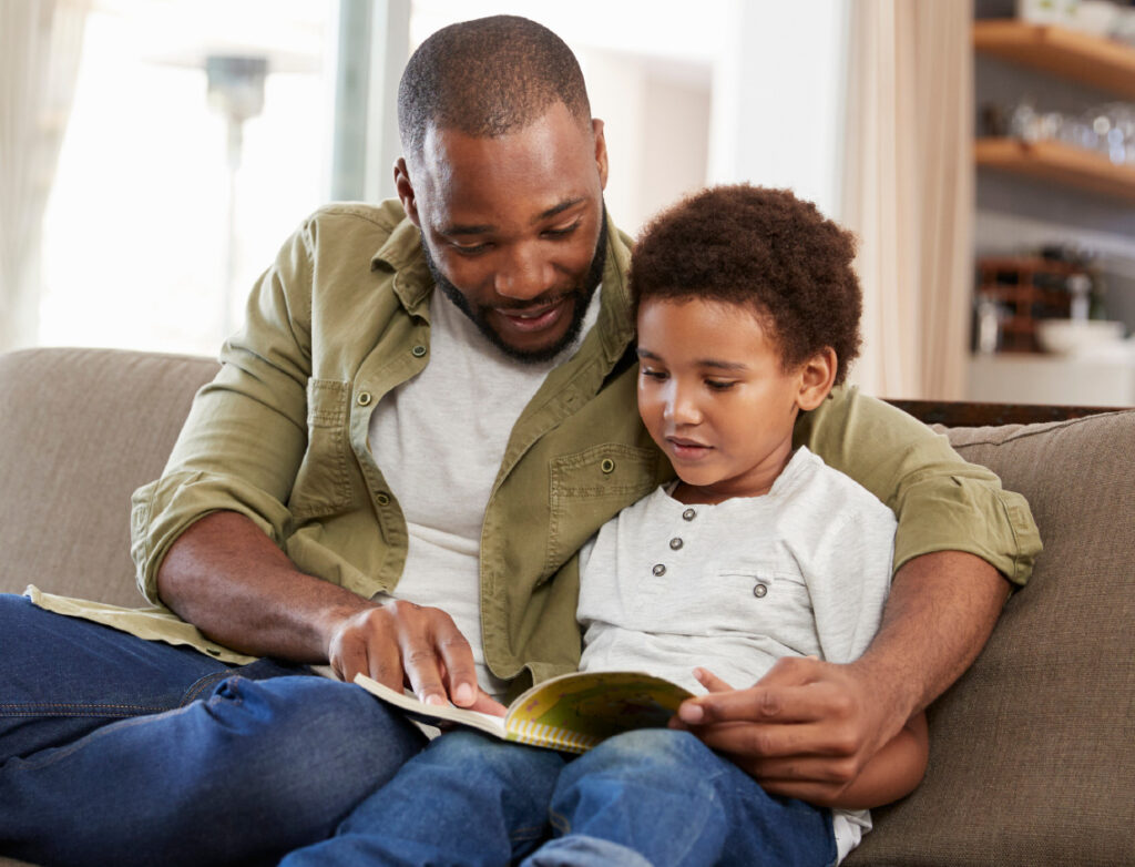 father and young boy reading on couch